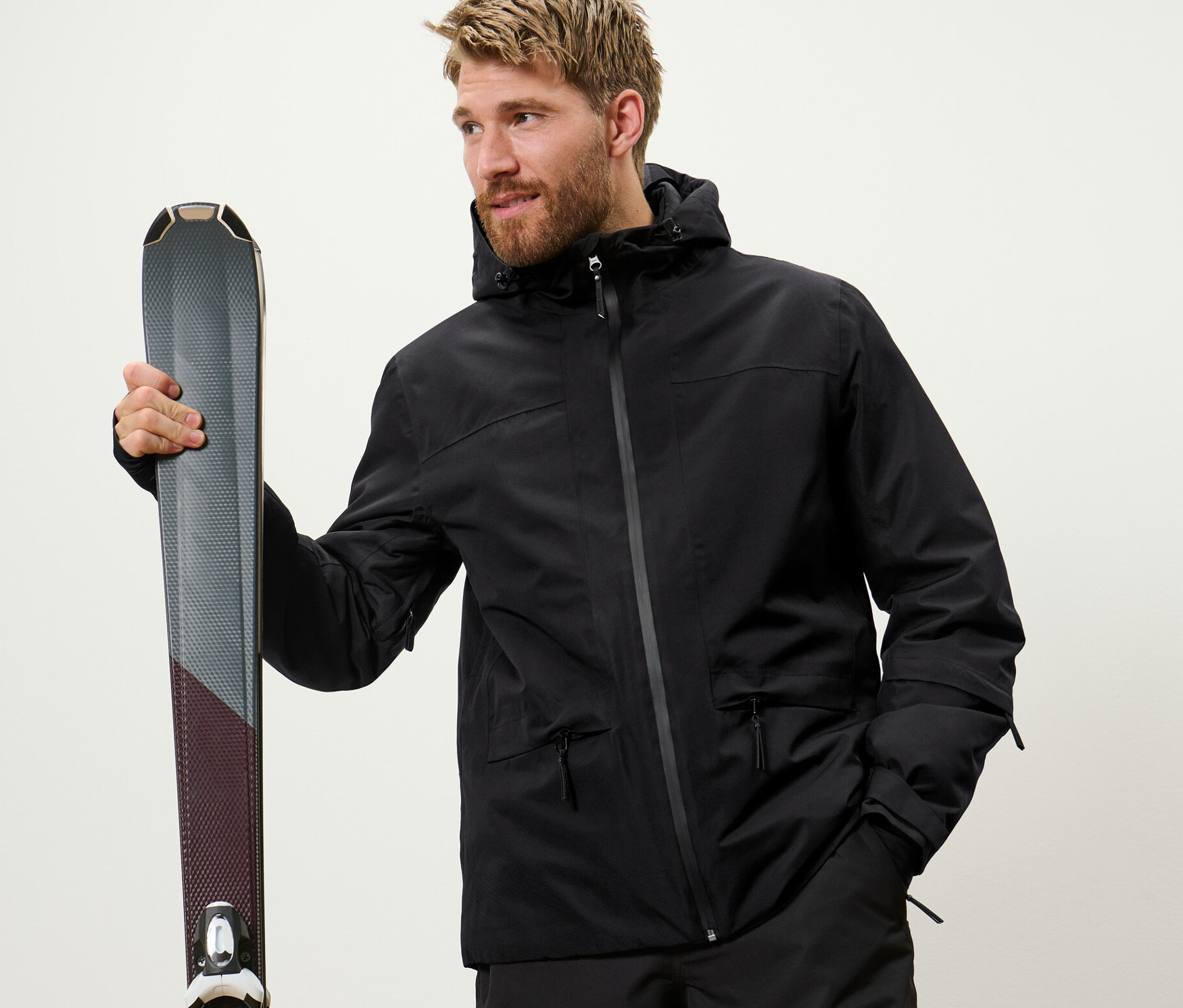 Mann hält Ski. Er trägt eine schwarze Skijacke.