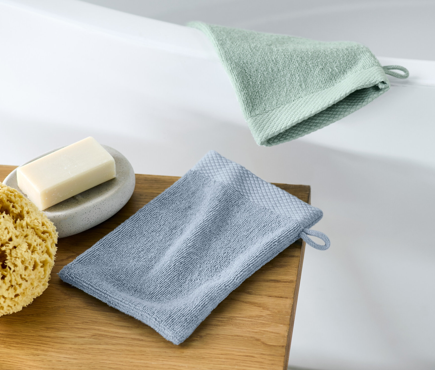 Zwei Waschlappen liegen auf einem Holzhocker neben Seife und einem Schwamm.