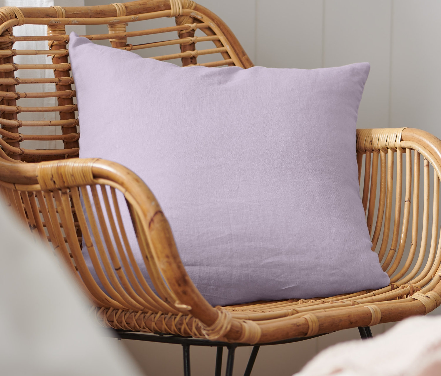 Ein Deko-Kissenbezug aus gewaschenem Leinen liegt auf einem Korbsessel.