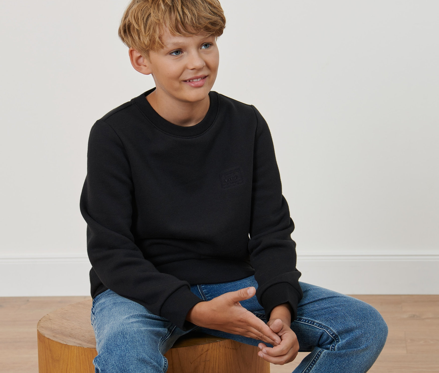 Ein Junge sitzt auf einem Hocker und trägt ein Kinder-Sweatshirt.