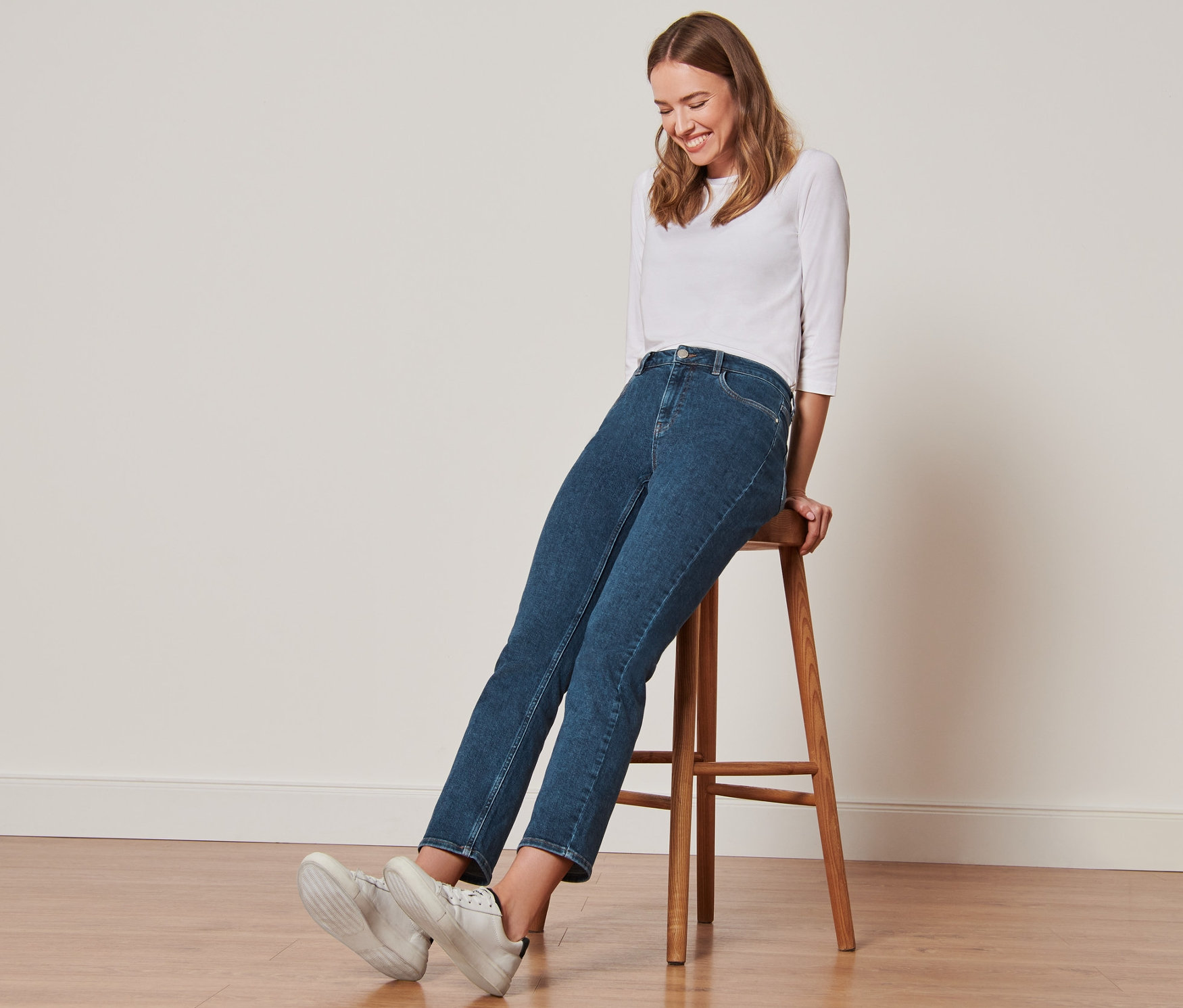 Frau sitzt auf einem Hocker und trägt Straightfit-Jeans.