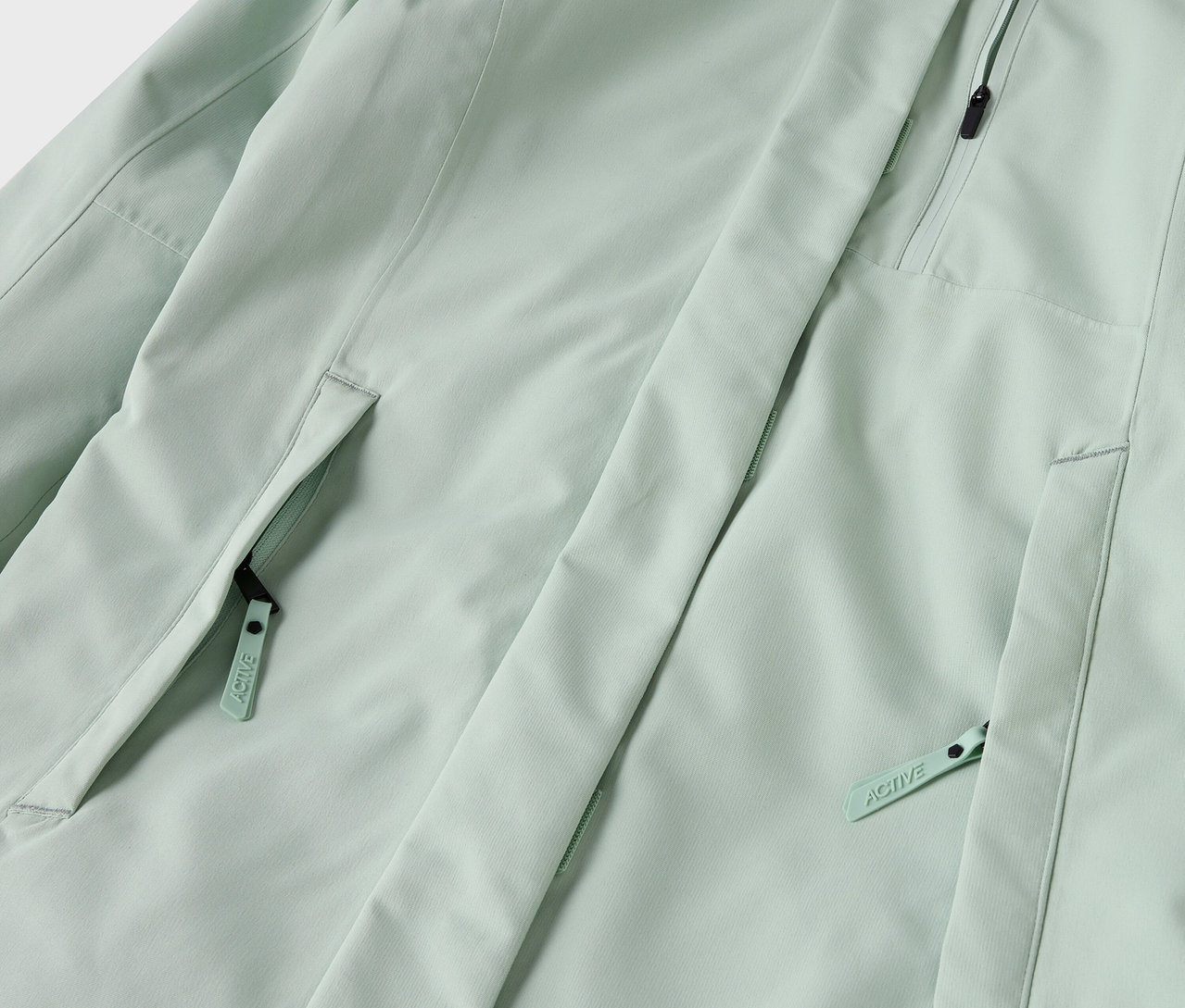 Detailaufnahme einer hellgrünen Jacke mit Reißverschlusstaschen.