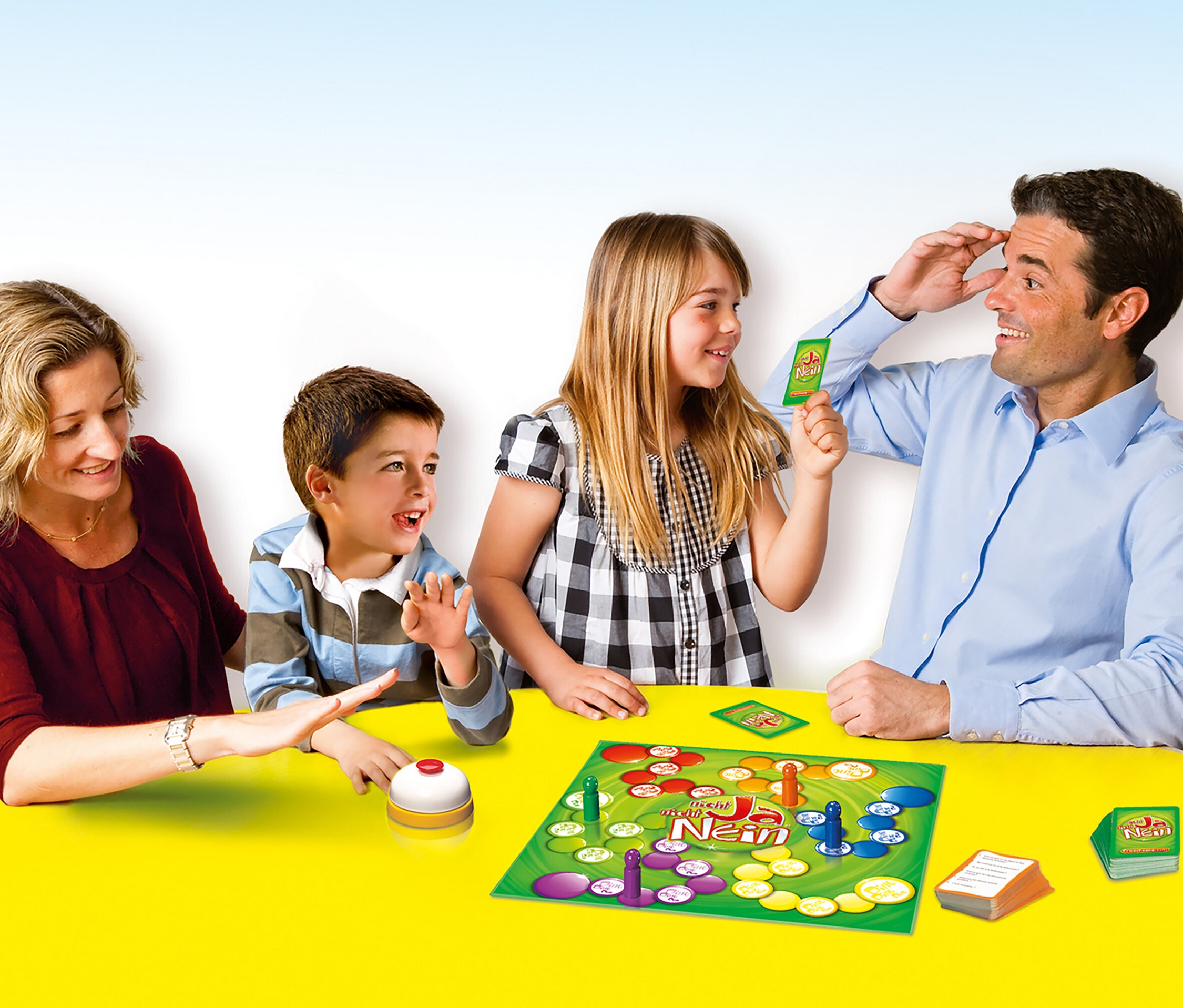 Vierköpfige Familie spielt das Spiel 'Spiel Nicht Ja, nicht Nein' auf einem gelben Tisch.