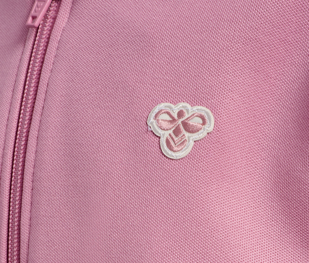 Detail einer rosa HUMMEL HMLJR Archive Reg Poly Zip Jacket mit Reißverschluss und Logo.
