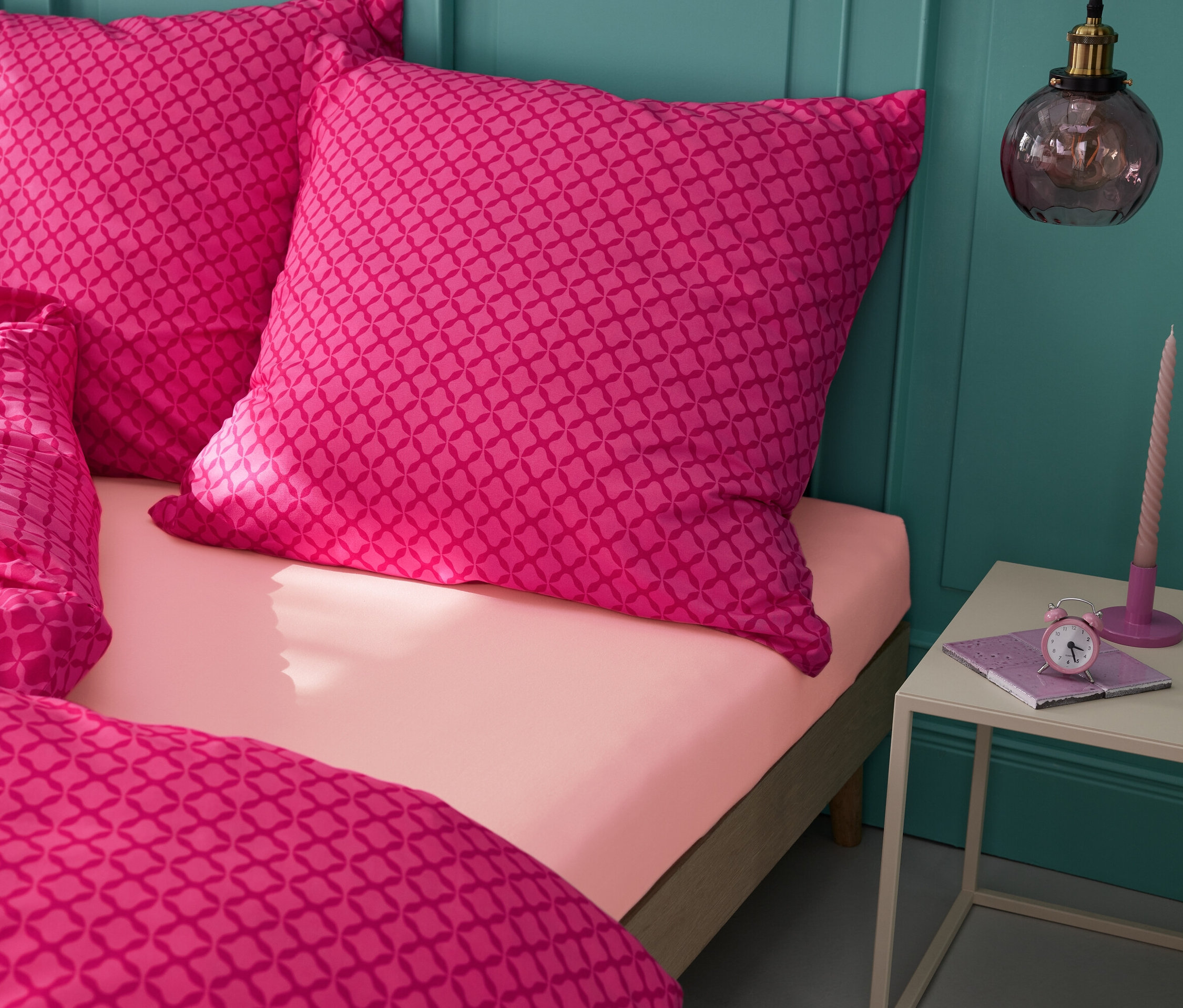 Bettwäsche und zwei Kissen mit geometrischem Muster auf einem Bett mit einem aprikosenfarbenen Jersey-Spannbettlaken.