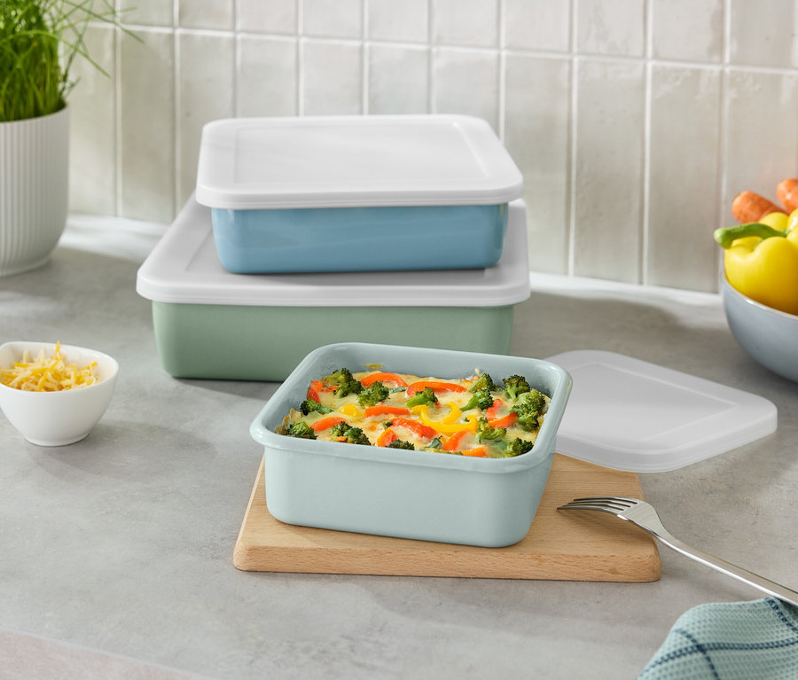 Gestapelte grüne und blaue rechteckige Behälter mit weißen Deckeln und eine kleine Schüssel mit geriebenem Käse.
