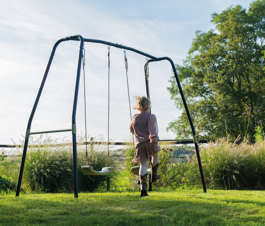 Mädchen steht auf der EXIT Doppelschaukel »Ivy« im Garten.