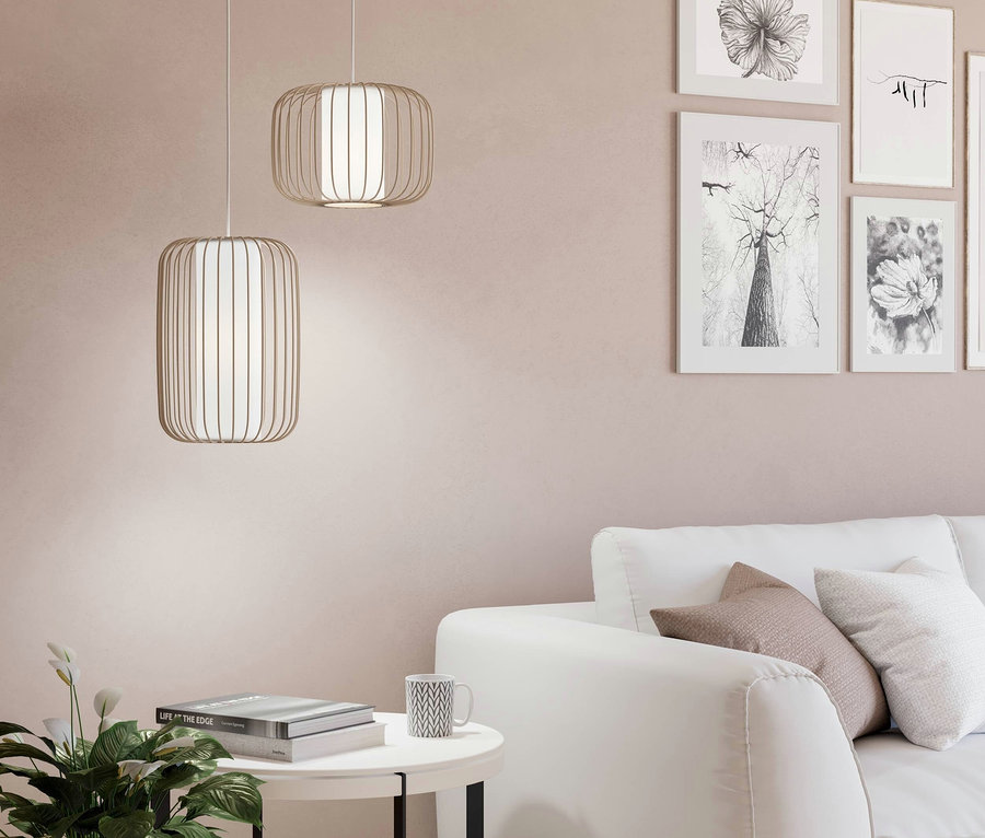 Zwei metallene Hängelampen über einem weißen Tisch mit Büchern und einer Tasse, im Hintergrund ein weißes Sofa und Bilder an der Wand.