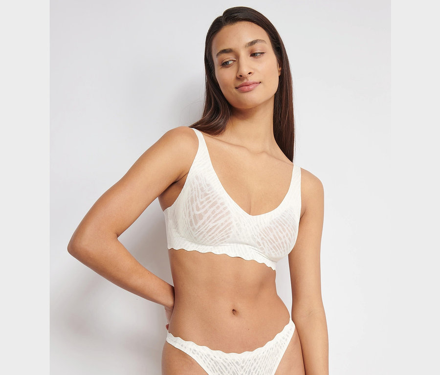 Eine Frau trägt einen sloggi ZERO Feel Bliss Soft Bra, silk white, und passende Slips.