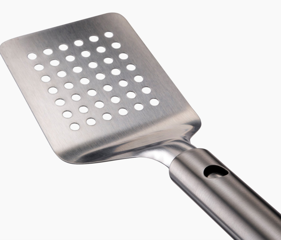 Nahaufnahme eines silbernen, gelochten Pfannenwenders vor einem weißen Hintergrund.