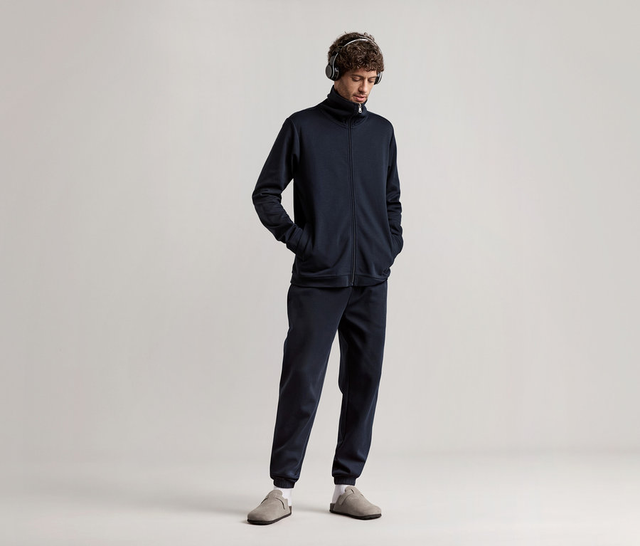 Mann mit Kopfhörern, der einen dunkelblauen Hausanzug trägt.