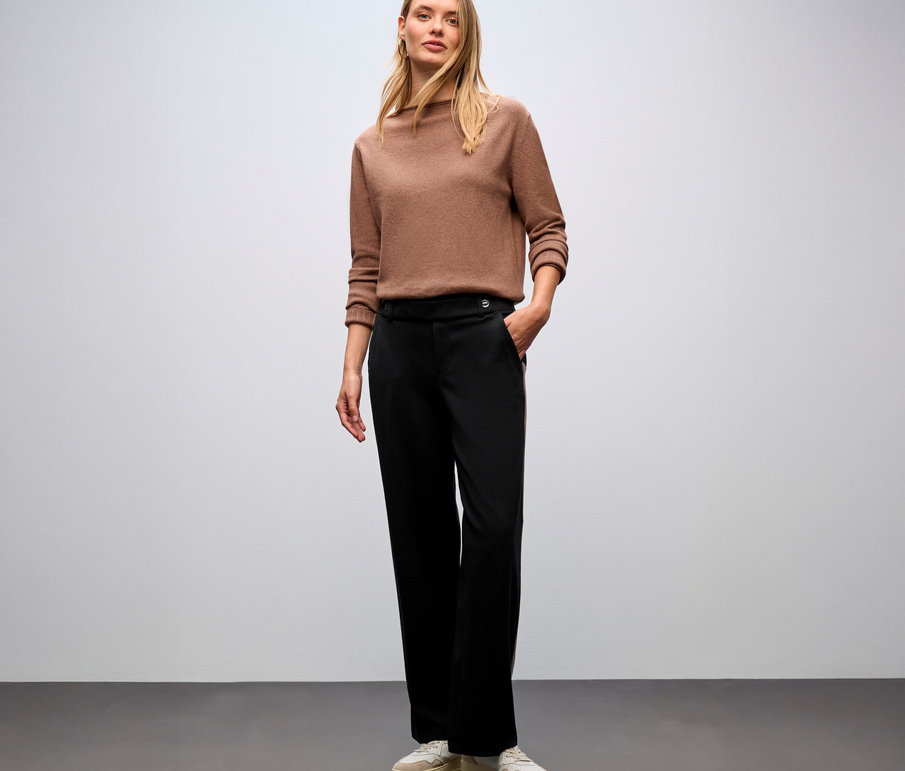 Frau steht und trägt einen braunen Pullover und eine schwarze Street One Straight Leg Hose mit Gallon.