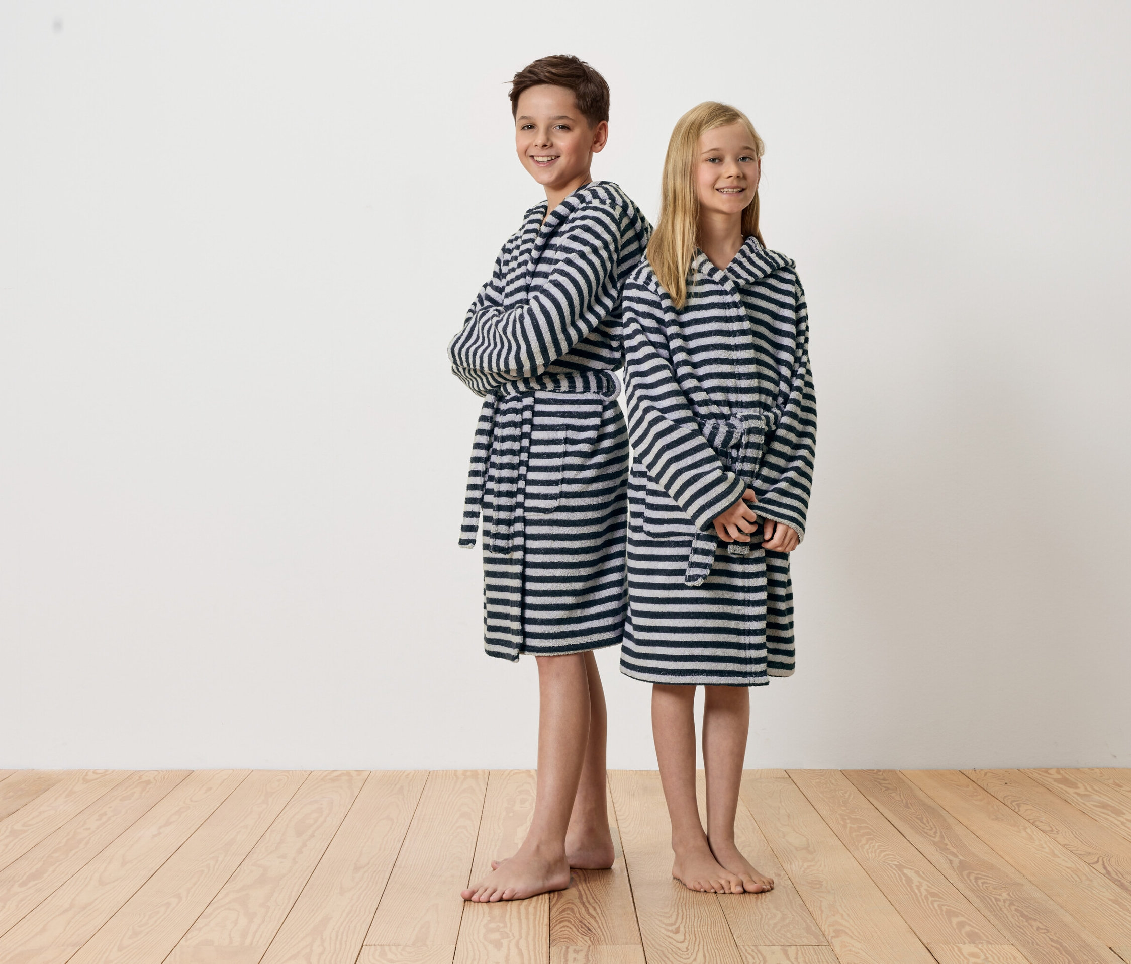 Ein Junge und ein Mädchen stehen Rücken an Rücken und tragen gestreifte Bademäntel.
