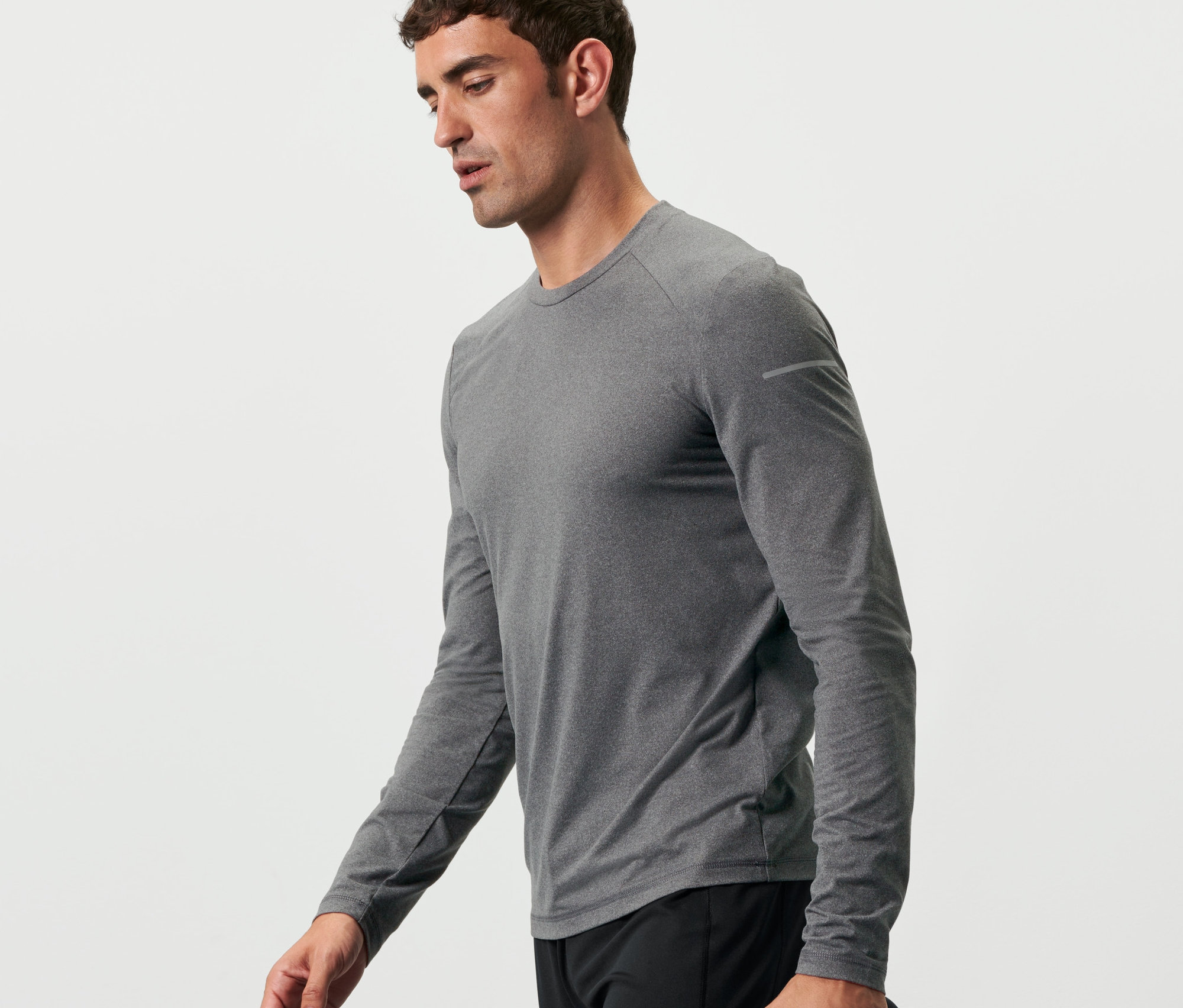 Mann geht und hält eine Wasserflasche. Er trägt ein meliertes, anthrazitfarbenes Langarm-Funktionsshirt.