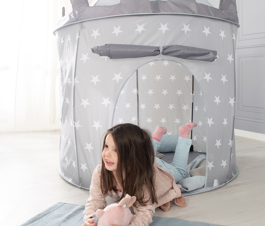 Mädchen liegt auf dem Bauch auf einem blauen Teppich und spielt mit einem rosa Stoffhasen. Dahinter steht ein graues roba Spielzelt "Ritterburg" mit weißen Sternen.