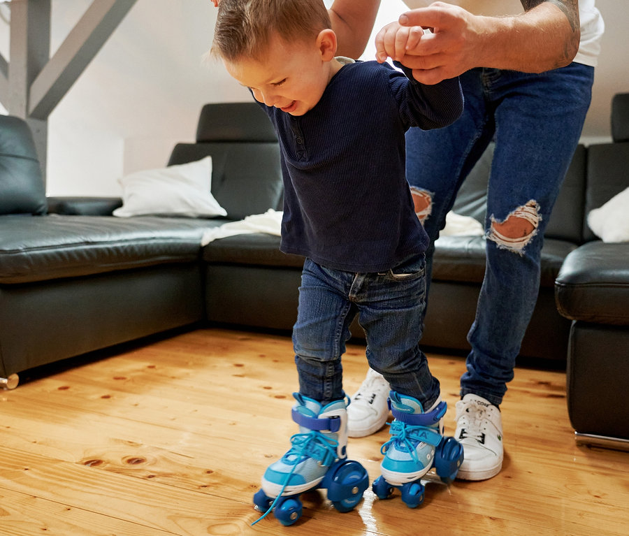 Vater hilft Sohn beim Rollschuhlaufen mit zyanfarbenen HUDORA »My First Quad« Rollschuhen.