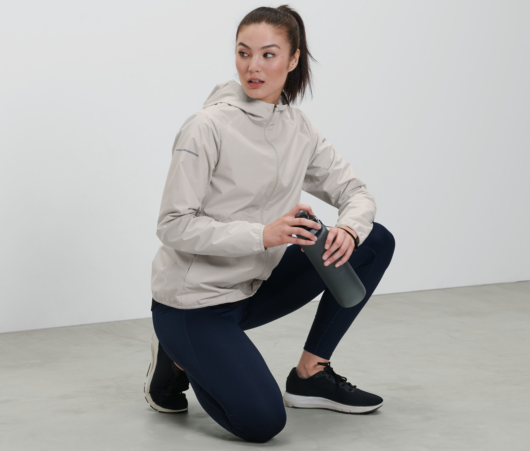 Frau in grauer Laufjacke hält eine Wasserflasche.