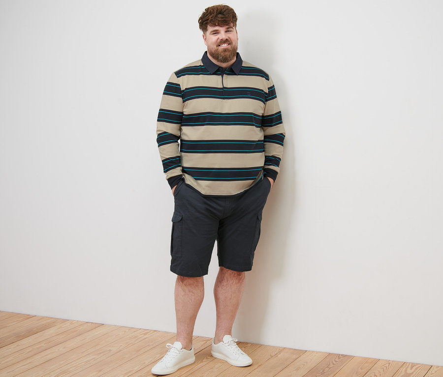 Ein Mann steht und trägt ein Langarm-Poloshirt, Shorts und Turnschuhe.