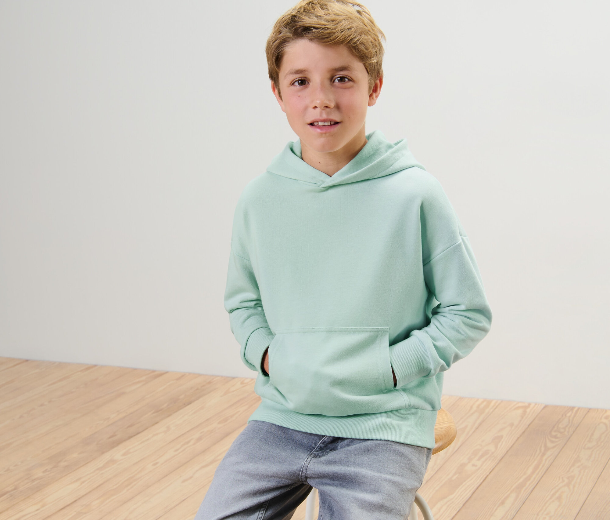 Junge sitzt auf einem Hocker und trägt einen Kinder-Sweat-Hoodie.