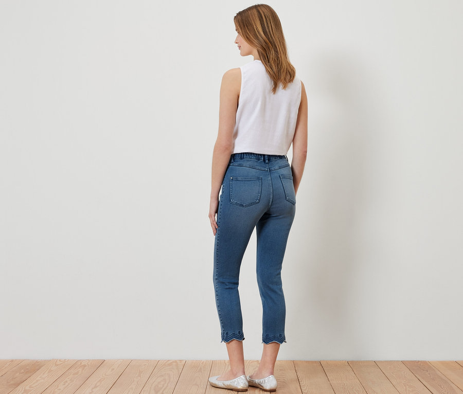 Frau von hinten trägt 7/8-Treggings mit Lochstickerei, ein weißes Top und silberne Ballerinas.