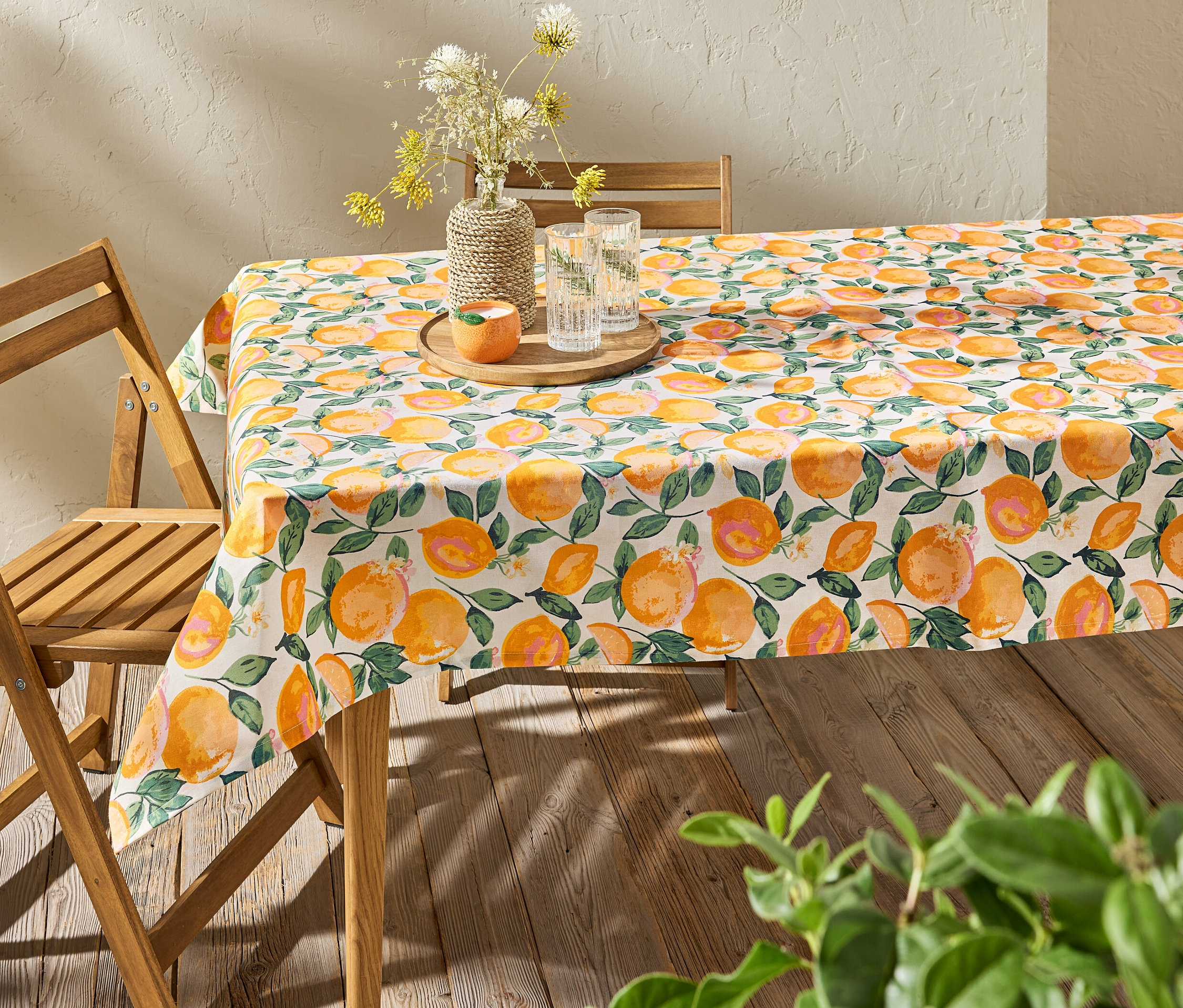 Tisch mit abwischbarer Tischdecke mit Zitrusmuster, darauf Vase mit Blumen und Wassergläser.