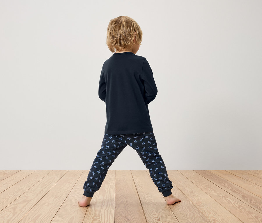 Junge von hinten, trägt dunkelblauen Langarmpyjama und gemusterte Hose.
