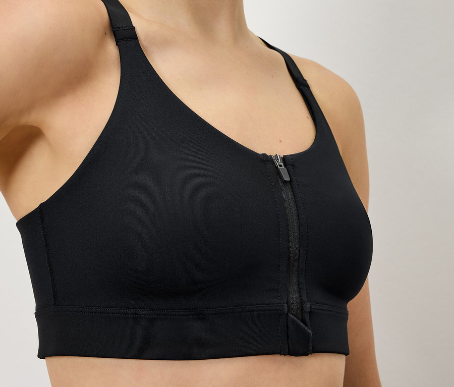 Frau trägt einen schwarzen Sport-BH mit Reißverschluss vorne.