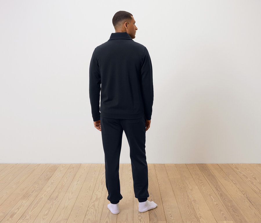 Mann von hinten trägt einen dunkelblauen Pyjama und weiße Socken.