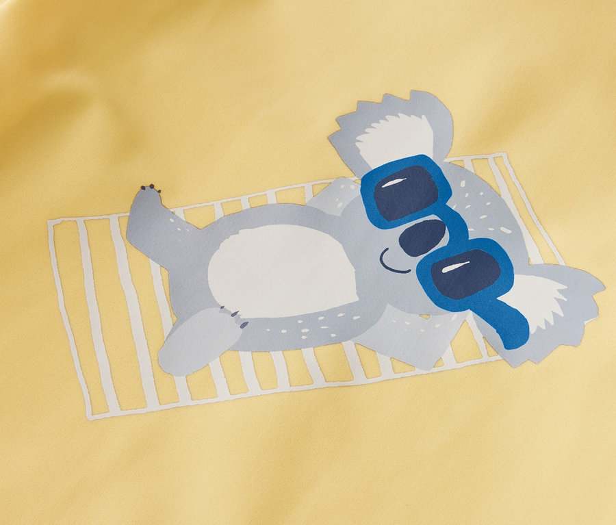 Gelbes Kinder-Shirt mit UV-Schutzfaktor 80, Koala liegt mit blauer Sonnenbrille auf einem Handtuch.