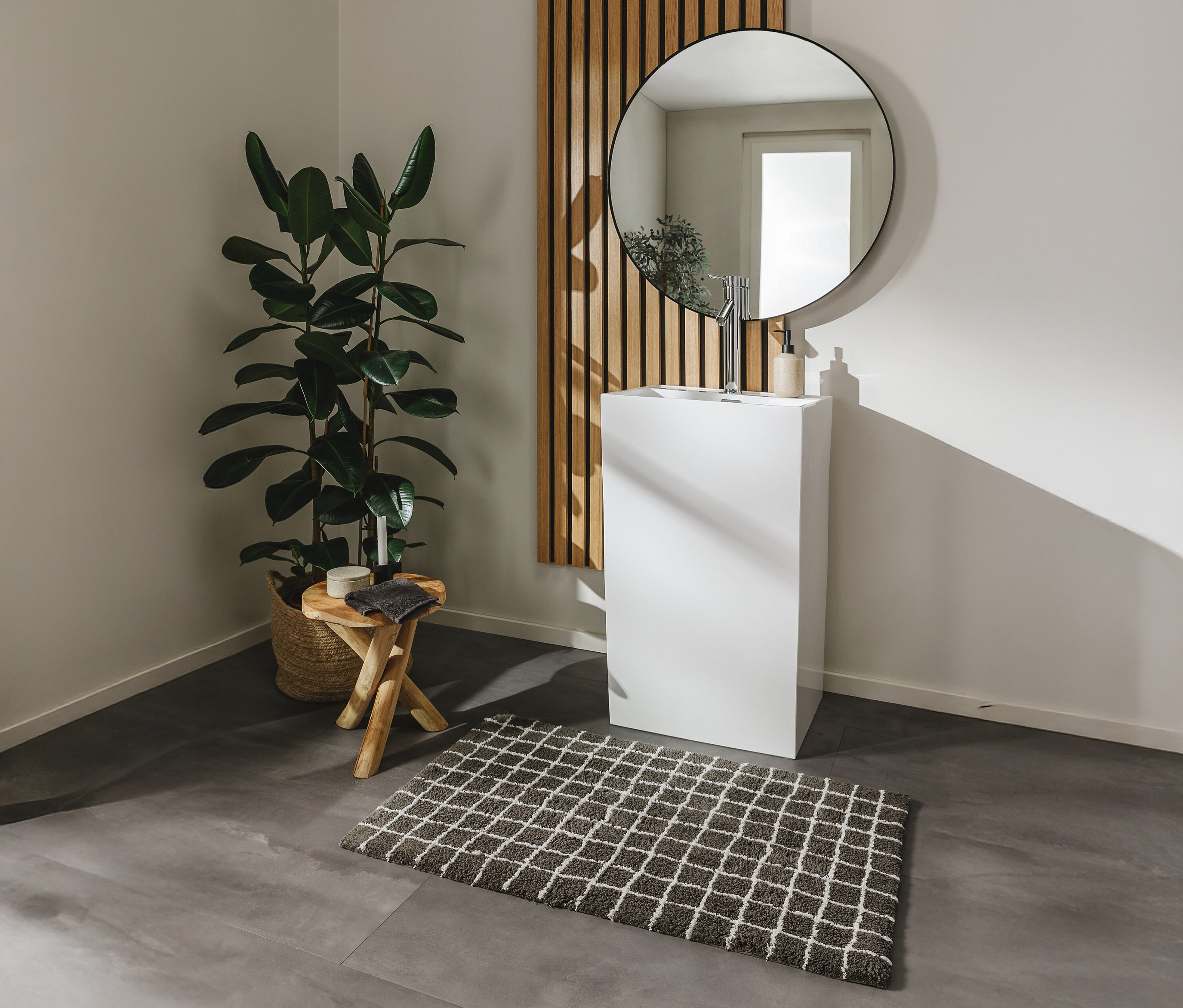 Eine graue Badematte »Wavu« von benuta (60 x 100 cm) liegt auf einem grauen Boden vor einem weißen Waschbecken.
