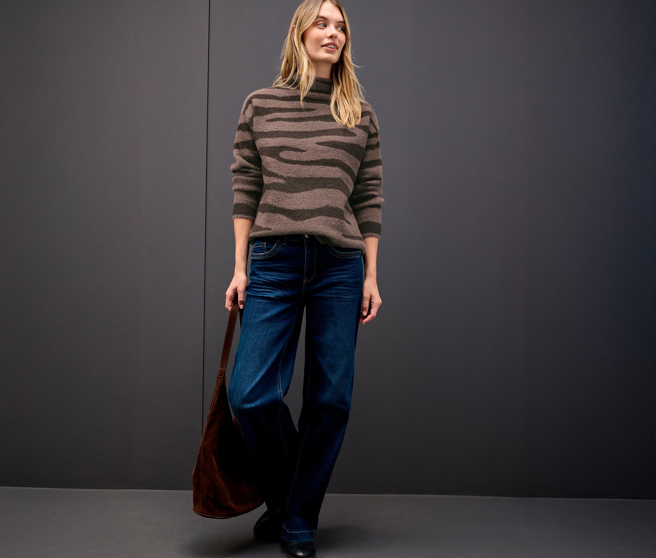 Frau trägt einen Street One Jacquard-Pullover, Jeans und eine Handtasche.