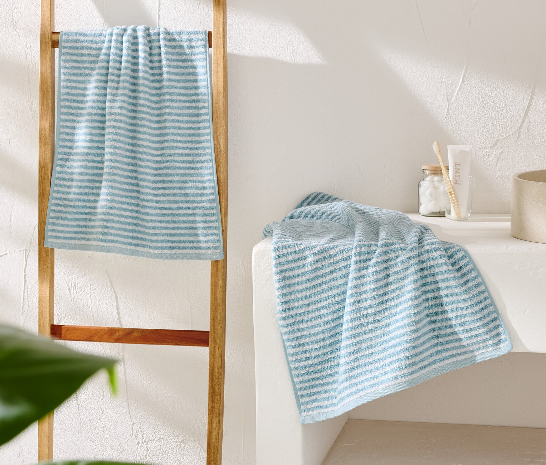 Ein blau-weiß gestreiftes Handtuch hängt an einer Holzleiter. Ein weiteres Handtuch liegt neben einem beigen Waschbecken.