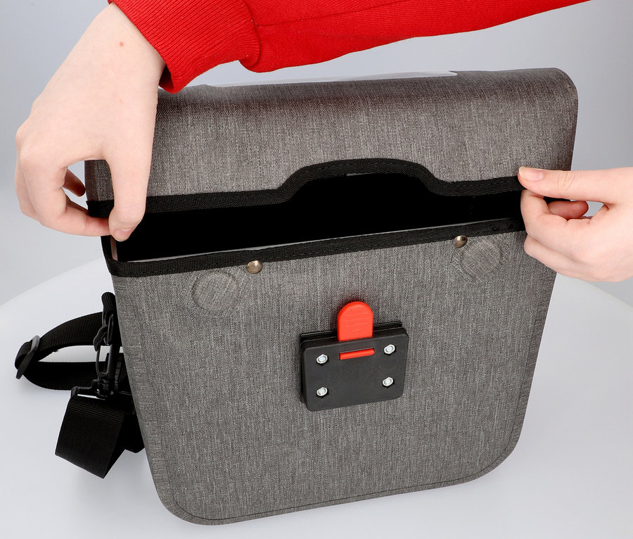 Eine Person öffnet eine graue Fahrradtasche, die auf einem Tisch steht.