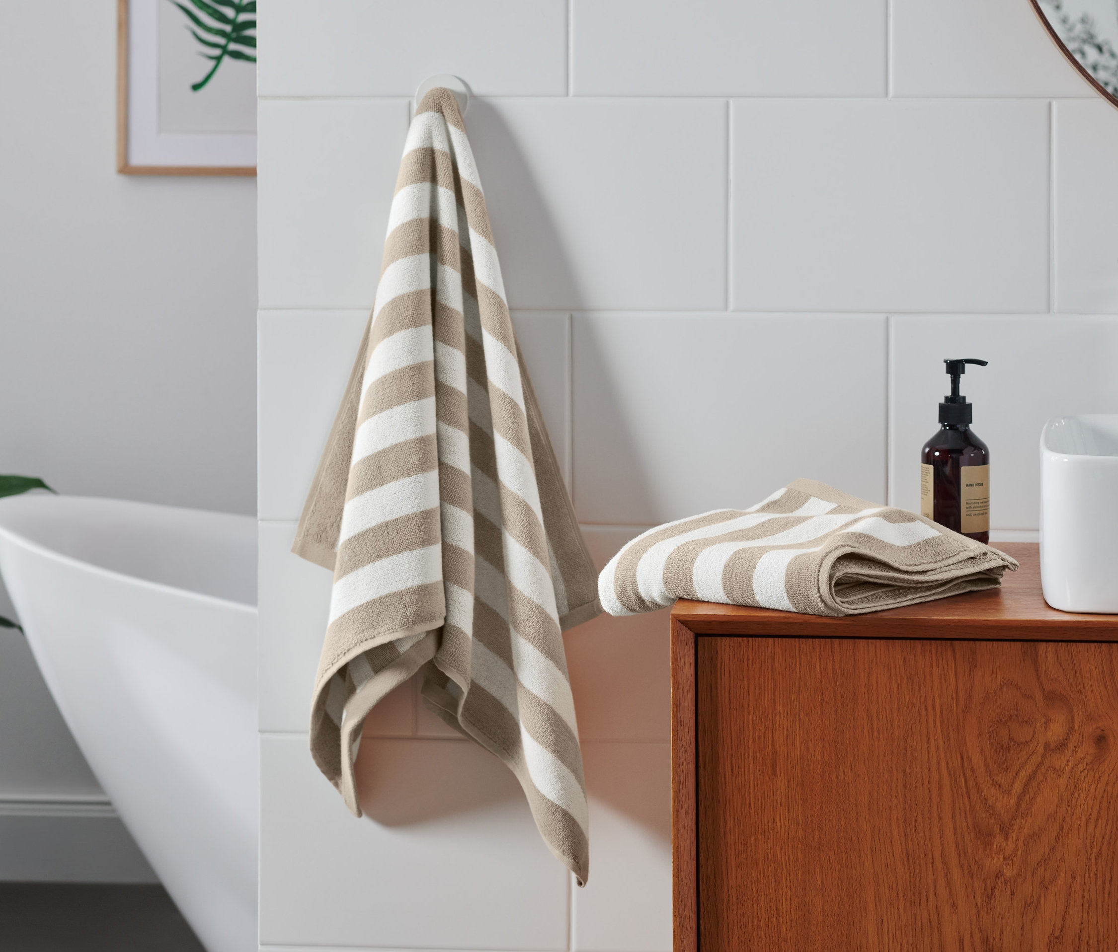 Im Badezimmer hängen und liegen zwei beige-weiß gestreifte Handtücher. Zwei hochwertige Handtücher, beige-weiß gestreift hängen an einem Haken, das andere liegt gefaltet auf einem Holzschrank.