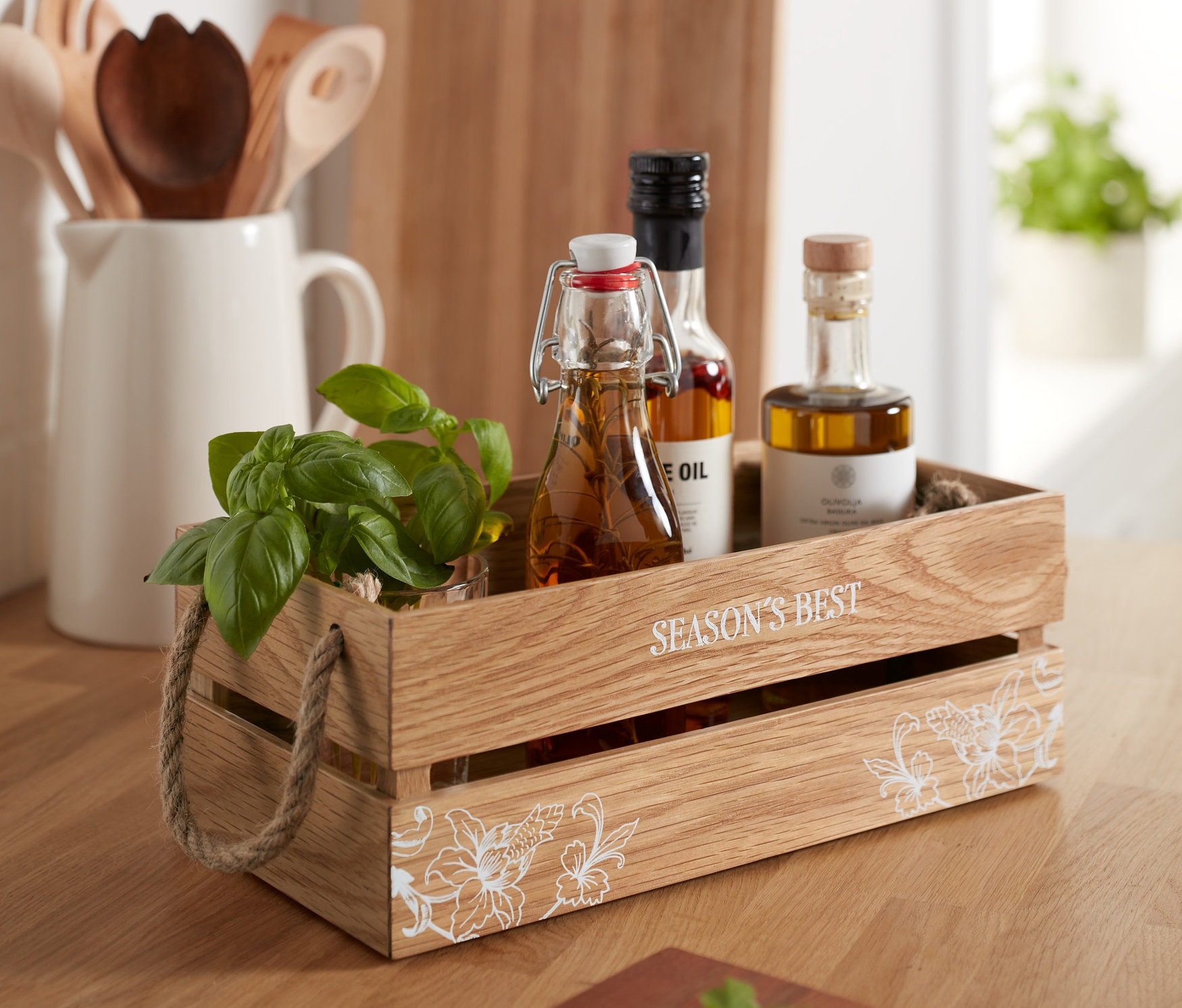 Dekorative Holzkiste mit Basilikum und drei Ölflaschen auf einem Holztisch.