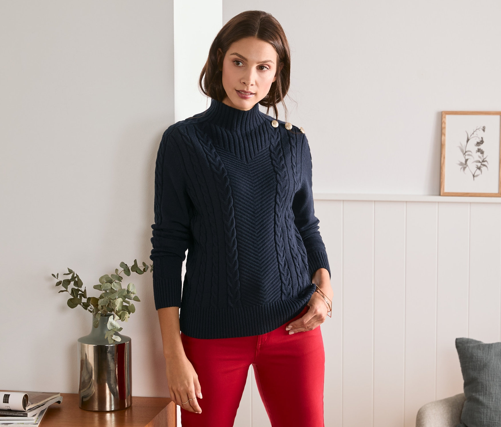 Frau posiert in blauem Strickpullover mit Knöpfen und roter Hose.