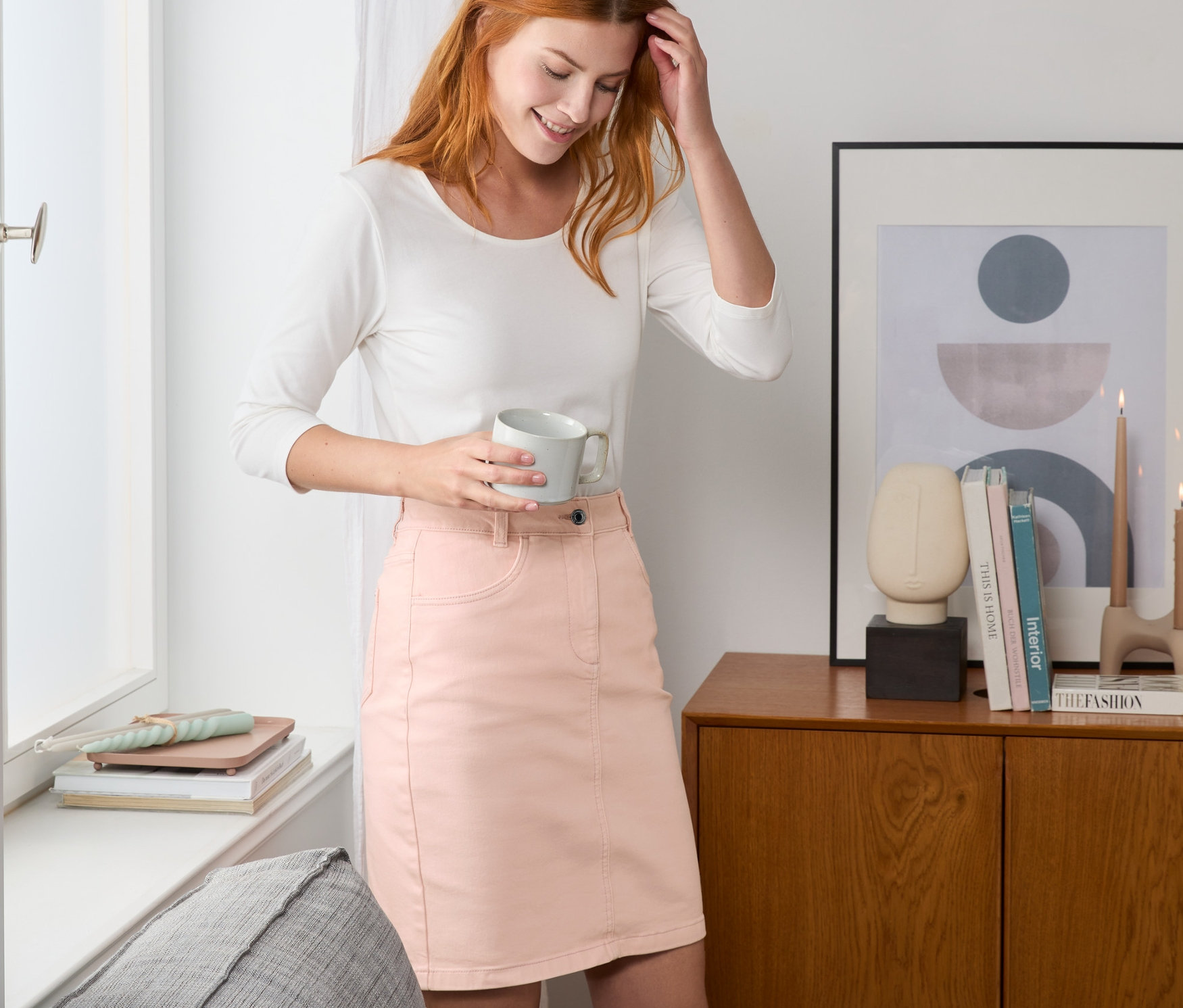 Frau hält eine Tasse und trägt einen roséfarbenen Jeansrock.