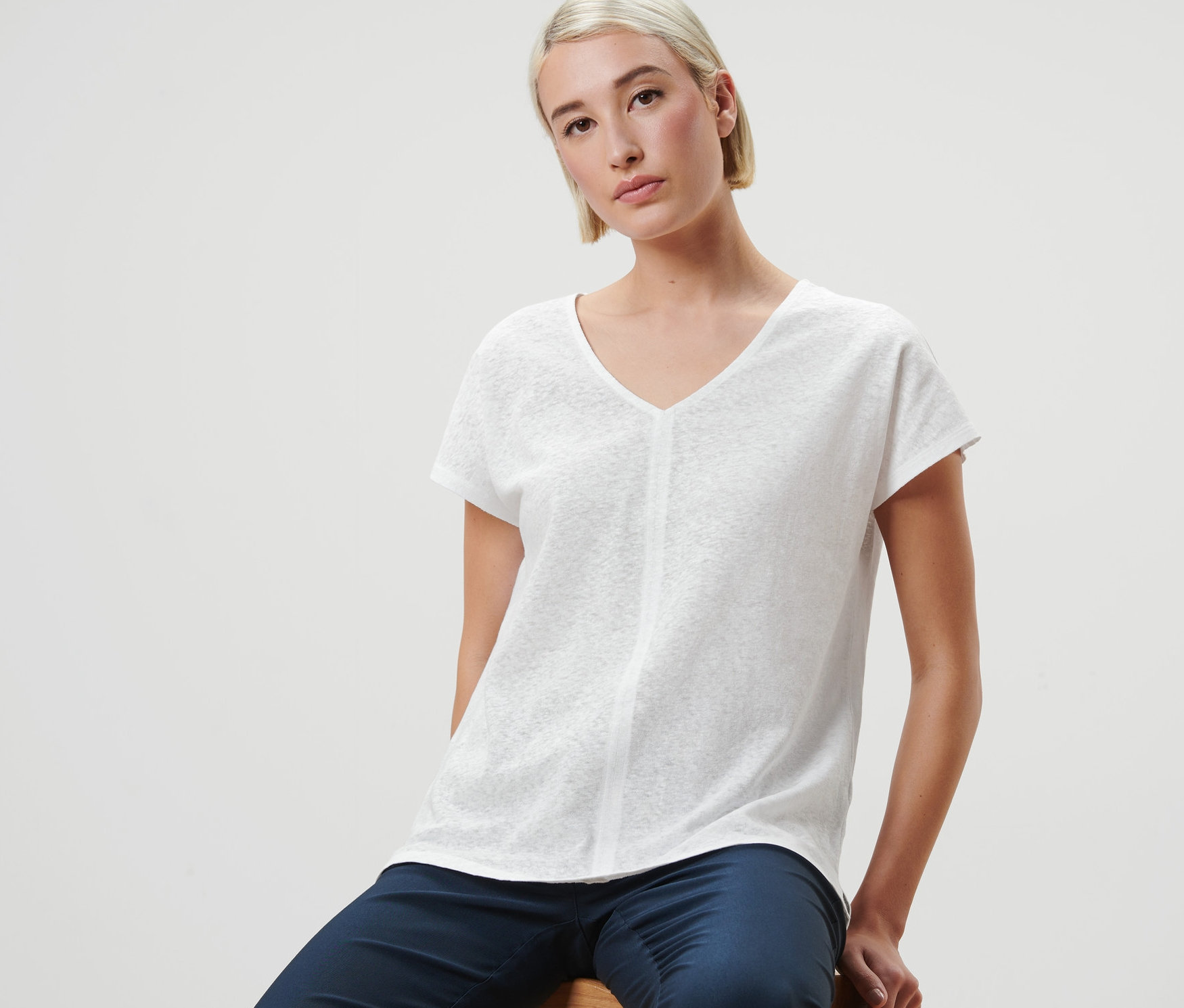 Frau sitzt auf Hocker und trägt cremeweißes Shirt mit Leinen.