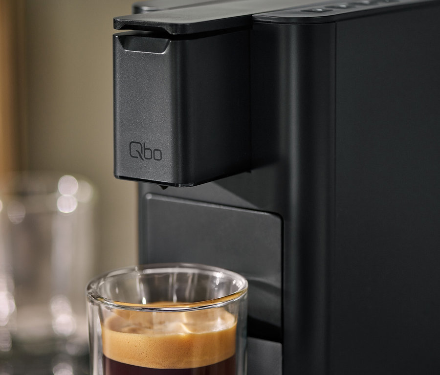 Detailaufnahme einer Qbo ICONIC Dark Chrome Kaffeemaschine mit einer Tasse Kaffee.