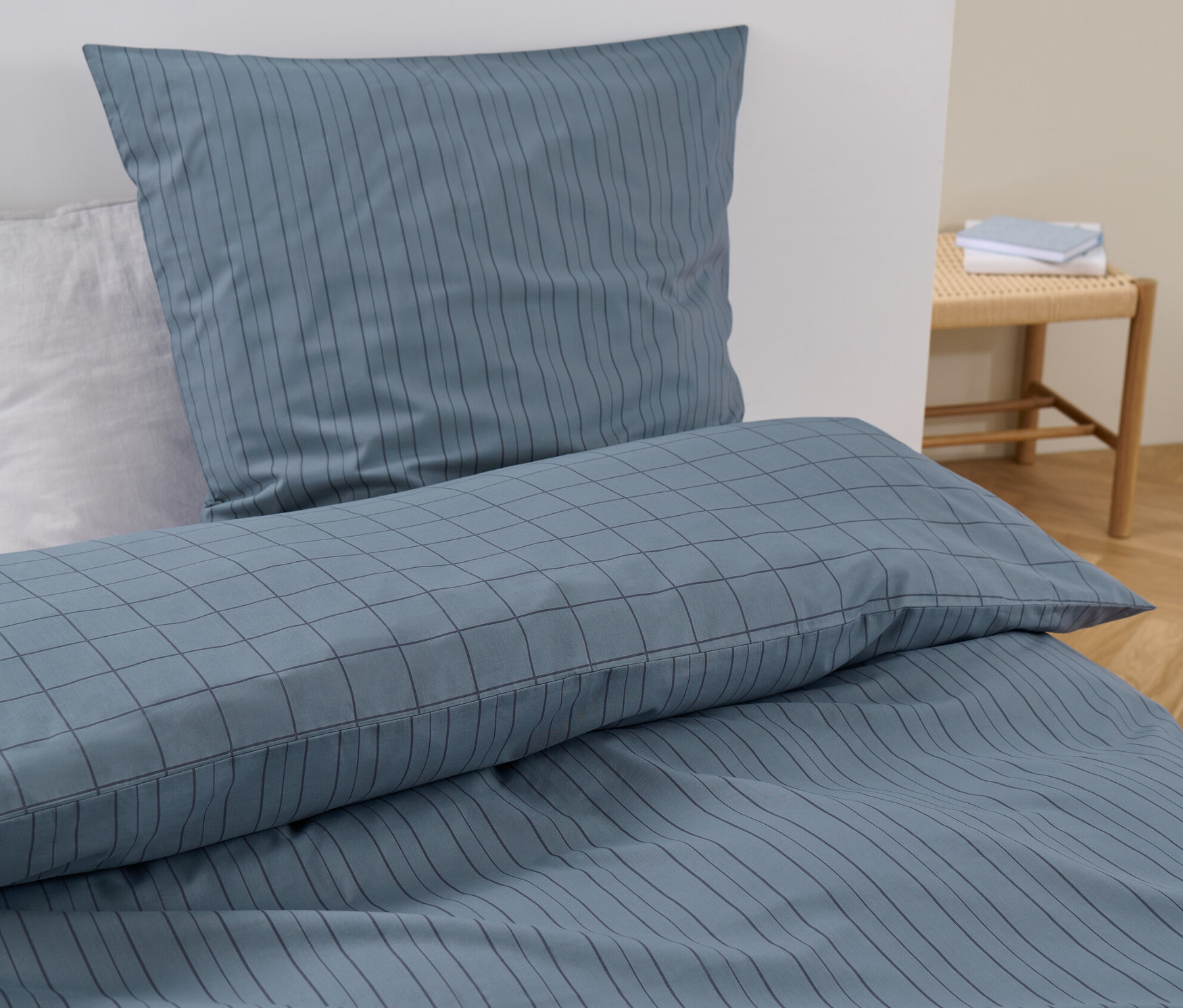 Blaue Renforcé-Bettwäsche Normalgröße mit Streifen und Karos auf einem Bett.