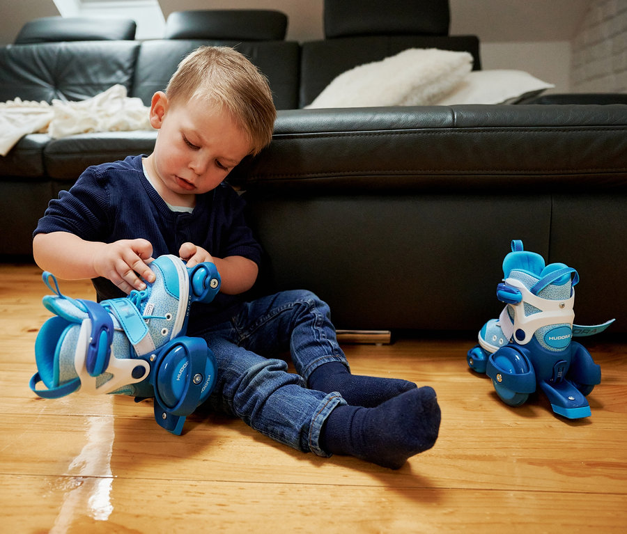 Ein Junge schnürt die Schnürsenkel an seinen blauen HUDORA My First Quad Rollschuhen.