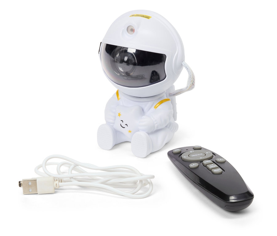 Ein weißer Nachthimmelprojektor in Form eines Astronauten sitzt neben einer schwarzen Fernbedienung und einem weißen USB-Kabel.