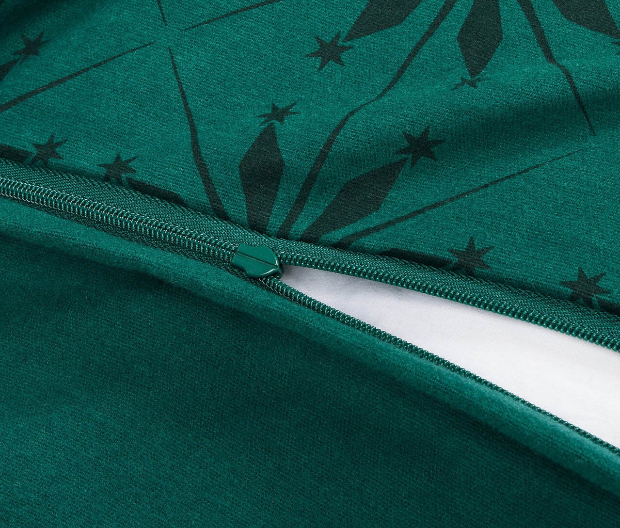 Detailansicht eines geöffneten Reißverschlusses auf einem grünen Bettbezug mit dunkelgrünem geometrischem Muster.