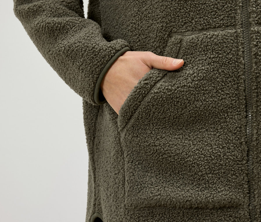 Hand in der Tasche einer olivgrünen Teddyfleecejacke.