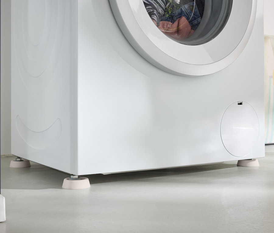 Detail einer weißen Waschmaschine, die auf weißen Unterlegscheiben auf einem grauen Boden steht.