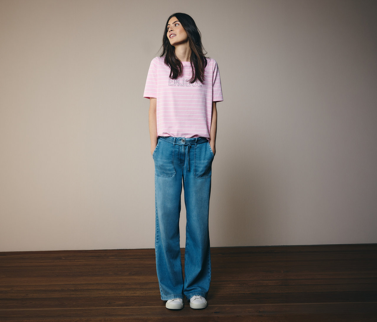 Frau mit den Händen in den Hosentaschen trägt ein CECIL Shirt mit rosa Streifen und Jeans.