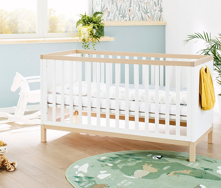 Ein Pinolino Babybett »Light« steht in einem Kinderzimmer mit Giraffen- und Pferdespielzeug.