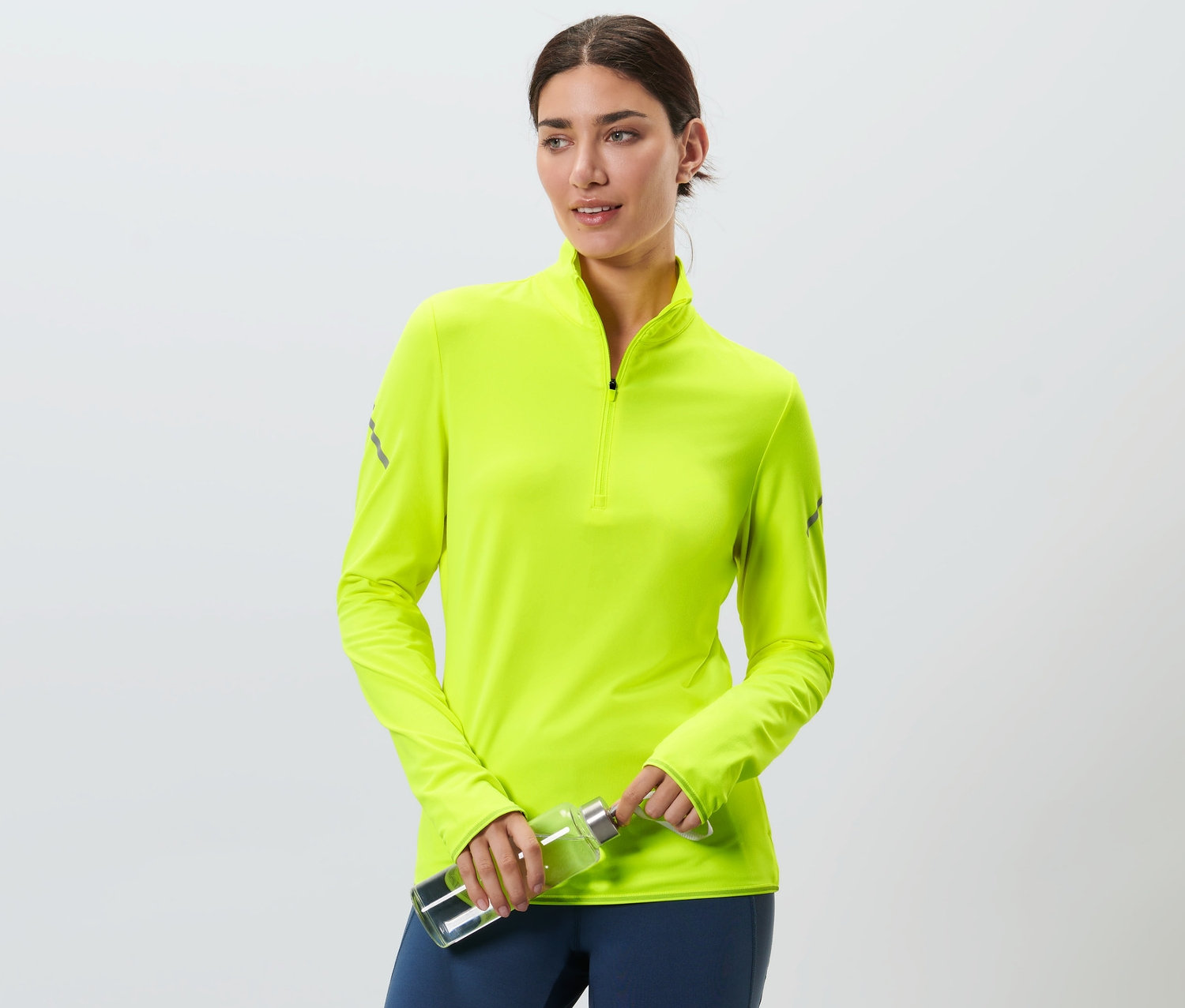Frau hält eine Wasserflasche und trägt ein neongelbes Thermo-Funktionsshirt.