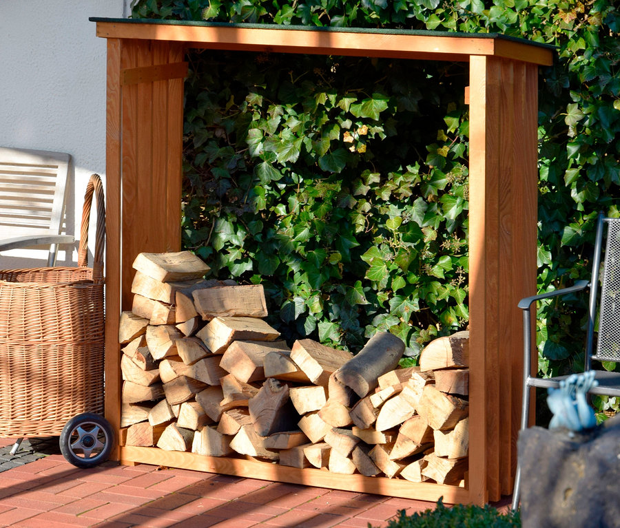 Ein Kaminholzregal, 15 mm, aus Kiefer, gefüllt mit Holzscheiten, steht draußen neben einem Weidenkorb.