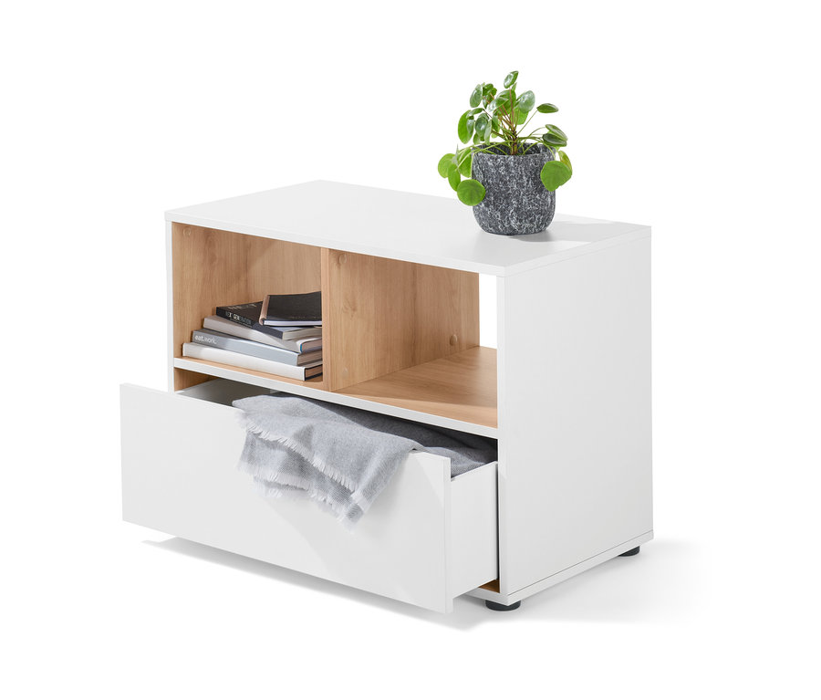 Weißes Sideboard mit Schublade, darauf eine Pflanze in einem grauen Topf. Im offenen Fach liegen Bücher, in der Schublade eine graue Decke.